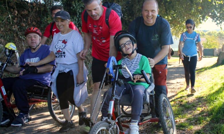 Personas disfrutando de un paseo con sillas de ruedas y apoyo de voluntarios en un entorno natural.